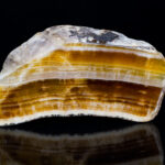 Examining Valence Electrons Cut polished aragonite gemstone with reflection on black background. Close-up of beautiful yellow, brown and white striped cross-section of mineral from Hridelec near Nova Paka in Czechia. Mineralogy.