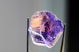 natural mined unheated Bolivian bicolor yellow purple ametrine raw rough crystal gem in tweezers closeup details inclusions look through massive