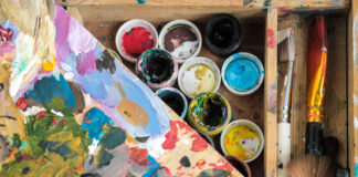 Paints of different colors and dirty brushes on an easel.