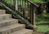Landscaping With Rocks: Ideas for Using Stone Outdoors Stone stairs with a metal handrail leading through a lush garden. The scene features a mossy stone retaining wall and green grass, highlighting peaceful outdoor landscaping with rocks