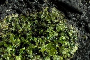 Close-up of gem quality small vibrant green peridot crystals with a few dark Olivine crystals