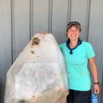rockhounding woman standing next to giant crystal as tall as her