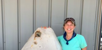 rockhounding woman standing next to giant crystal as tall as her