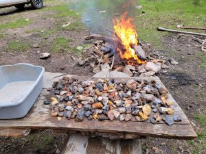 table covered with rocks found while rockhouding with a campfire in the background