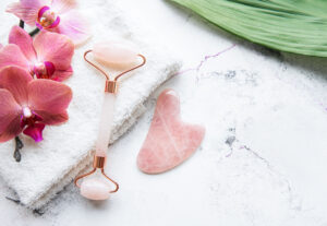 Rose quartz face roller for facial massage with towel and orchid flowers on a marble background