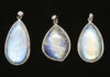 Three moonstone pendants with blue adularescence displayed on a black background