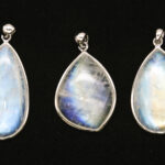 Moonstone Field Guide: Facts & Uses Three moonstone pendants with blue adularescence displayed on a black background