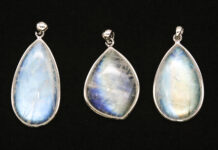 Three moonstone pendants with blue adularescence displayed on a black background