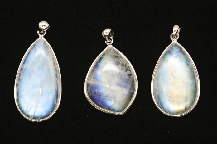 Three moonstone pendants with blue adularescence displayed on a black background