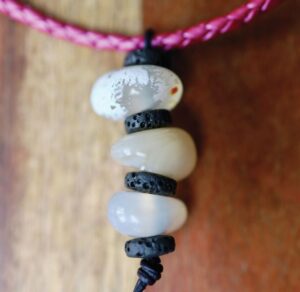 a beaded necklace with white beads and lava beads strung on a pink leather cord