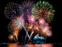 Beautiful colorful fireworks display showing on the sea beach with multi color of reflection on water.